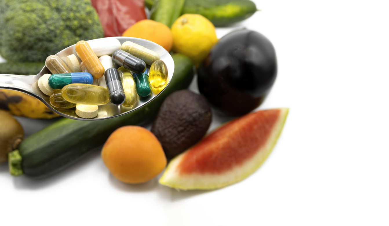 Capsules and pills of nutritional supplements and fresh vegetables and fruits background, concept of healthy life and supplementation