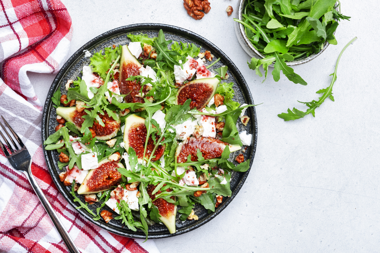 Delicious summer salad with sweet  figs, white feta cheese, walnuts, arugula and jam vinegar dressing on white table background, top view, negative space