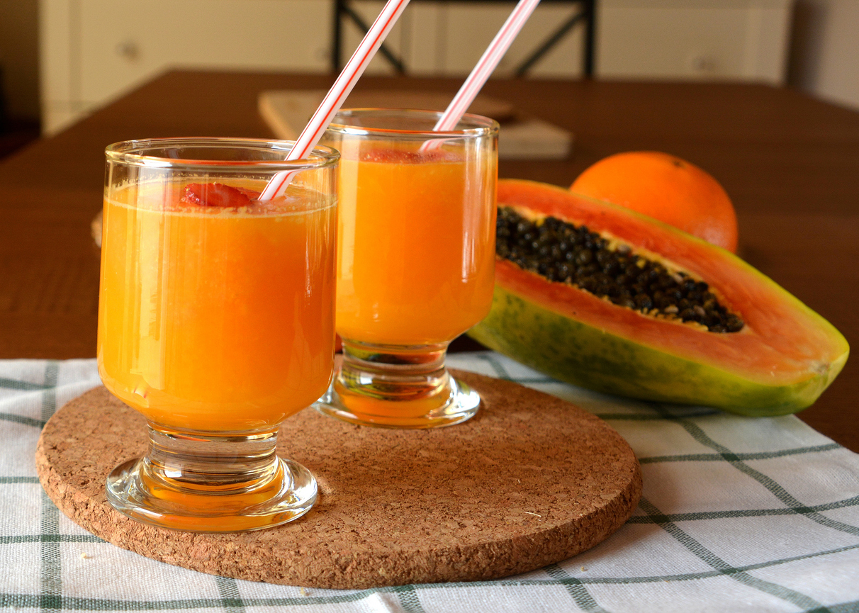 Two glasses of fresh orange and papaya smoothie on a wooden table.