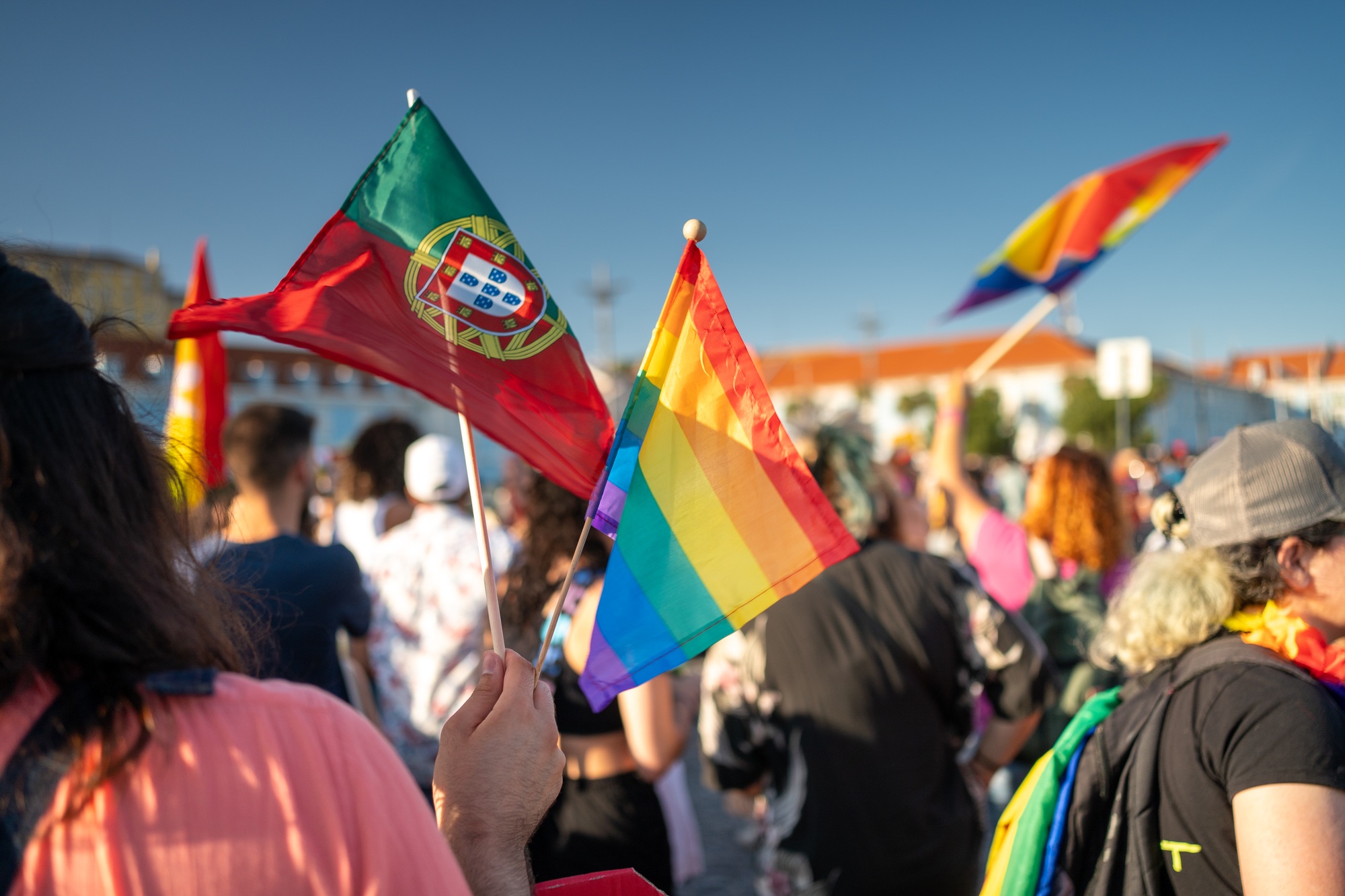 LGBTQ person holding flags of Portugal and rainbow at Pride Parade